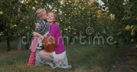 微笑的女儿和母亲拥抱在一个苹果园4k视频的预览图