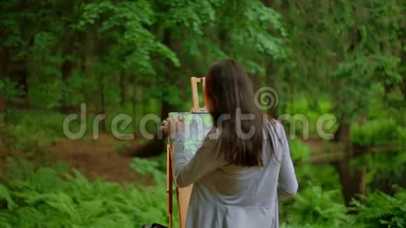 一位年轻的艺术家女士在夏日森林中描绘风景的后景视频的预览图