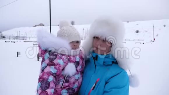 在冬天妈妈抱着她的小女儿在雪道上散步家长与孩子在公园散步视频的预览图