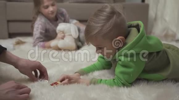 两个可爱的孩子躺在地板上毛茸茸的地毯上在家玩他们的玩具男性手抚摸玩耍的孩子视频的预览图