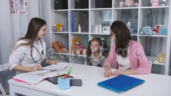 妈妈和小女儿去看医生一个女人带着一个小女儿在孩子的办公室接受检查视频的预览图