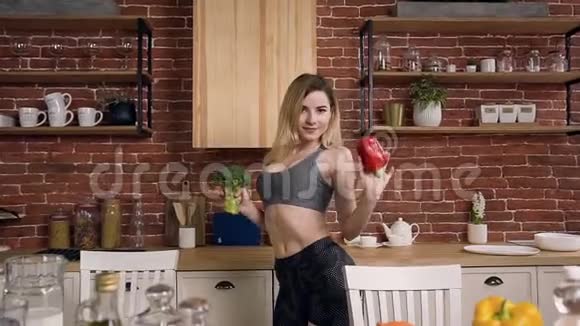 漂亮的运动女孩在厨房里跳舞手里拿着胡椒和西兰花视频的预览图