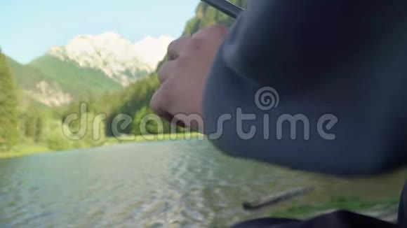 在湖边一个阳光明媚的日子里一个人拿着鱼竿鱼卷或垂钓者的缓慢动作有山有湖视频的预览图