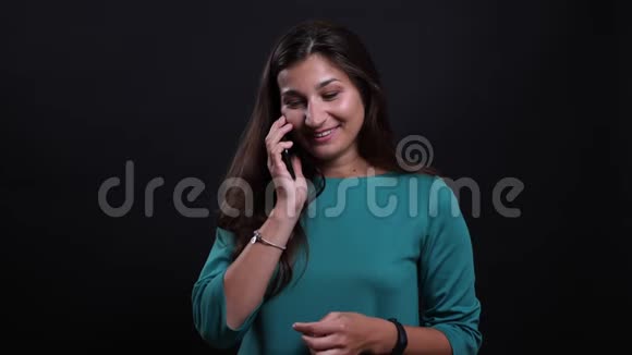 一位年轻漂亮的黑发女性的特写照片她打电话看着一架背景与黑色隔离的照相机视频的预览图