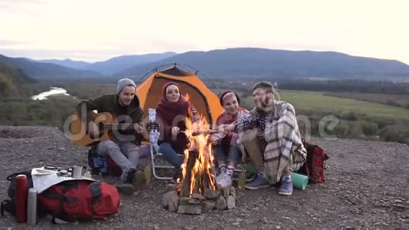 年轻的旅行者在弹吉他他的朋友们在山上日落时烤香肠友谊视频的预览图