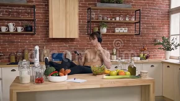 美丽的健康男孩听音乐吃胡萝卜同时上网在智能手机在家里视频的预览图