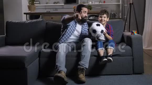 令人兴奋的爸爸和儿子在家电视上看足球视频的预览图