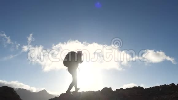 一位年轻女子徒步旅行的剪影背着背包走上山顶迎着蓝天和晚霞视频的预览图