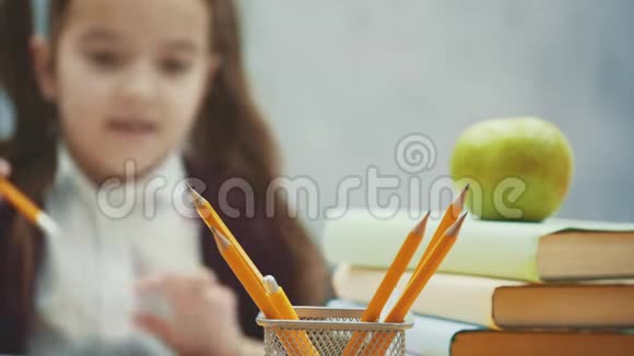 一个漂亮的女学生在灰色背景下坐在桌子旁在此期间需要一支黄色的铅笔视频的预览图