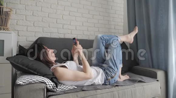 年轻女子躺在沙发上在智能手机上进行网上购物网上购物的概念视频的预览图