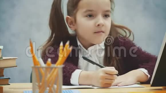 一个好的女学生坐在灰色背景的桌子旁在这篇写作中作业跳舞微笑动作缓慢视频的预览图