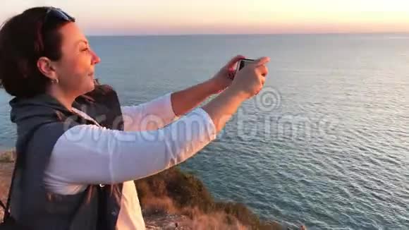 站在悬崖上的女人拍了一张海上日落的照片视频的预览图