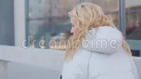 金发女人在寒冷的阳光下走在城市的街道上转向镜头调情玩弄头发视频的预览图