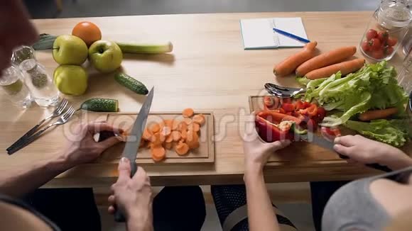 将男人切胡萝卜和女人切胡椒放在厨房背景的木切割板上视频的预览图