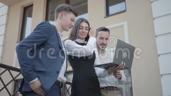 肖像年轻女子和两名男子在正式穿着讨论项目的笔记本电脑在露台上业务关系视频的预览图