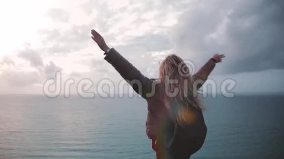 一个年轻女子背着背包在诺曼底海边的悬崖上享受风她举起双手视频的预览图