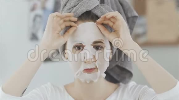 美丽的女孩头上有毛巾前镜摘去保湿面膜视频的预览图