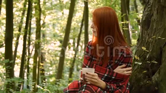 在公园或森林里喝咖啡或杯子里的茶的年轻女人视频的预览图