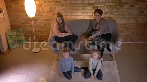 在舒适的家庭氛围中白种人的母亲和三个女儿坐在沙发上看电影视频的预览图