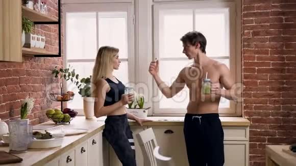 漂亮的运动男人手里拿着冰沙把他的肌肉放在手臂上给厨房里漂亮的女人看视频的预览图