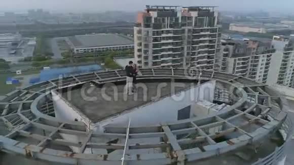 日落时分在现代公寓大楼楼顶拍摄的拥抱情侣的空中轨道镜头视频的预览图