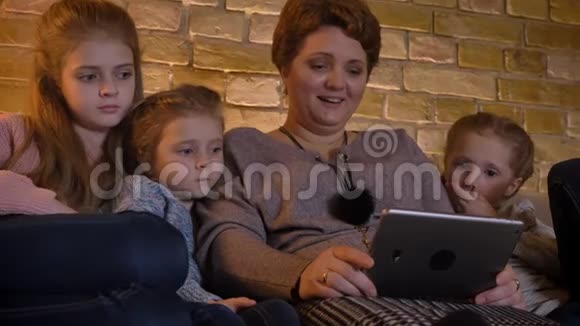 白种人母亲和女儿的家庭肖像在舒适的家庭氛围中带着笑声观看平板电脑视频的预览图