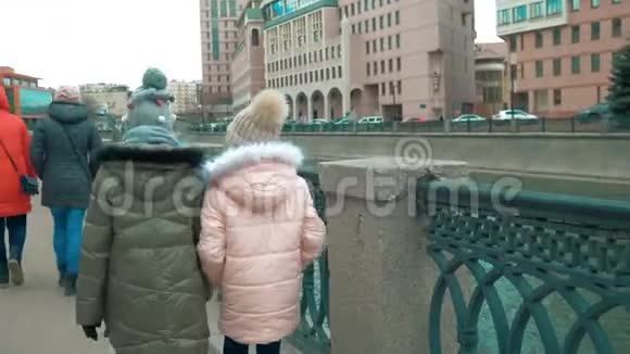 有妈妈的女孩在城市建筑背景下的城市堤上行走视频的预览图
