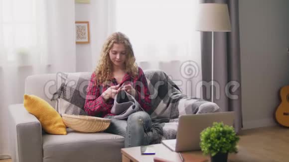 坐在沙发上在舒适的家编织衣服的迷人女人的恐慌视频的预览图