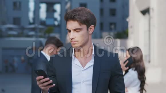年轻人使用智能手机的肖像和一群商业人士在后台讨论工作在工作中视频的预览图