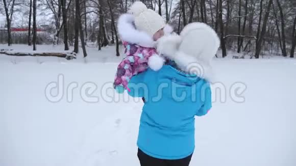 妈妈双手抱着小宝宝走在冬天的雪道上女儿在妈妈手里笑家长服务视频的预览图