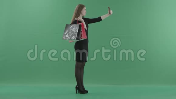 穿着黑色小裙子的漂亮女人拿着购物袋在手机上自拍她是视频的预览图