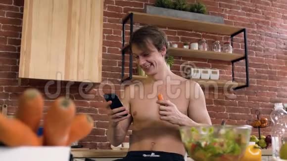 在家里用智能手机上网的时候一个很有魅力的运动男人正在吃胡萝卜视频的预览图