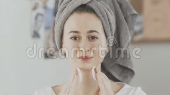年轻女子头上有毛巾用棉垫洗脸看着相机视频的预览图