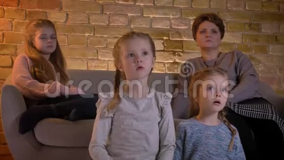 白种人母亲和三个女儿坐在一起在舒适的家中专心看电影的家庭画像视频的预览图