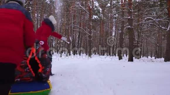 孩子们骑着爸爸的雪橇和充气雪管快乐的一家人在冬季公园和森林里玩耍视频的预览图