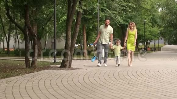 妈妈和爸爸小儿子一起在公园散步夏天带着孩子们滑板车视频的预览图