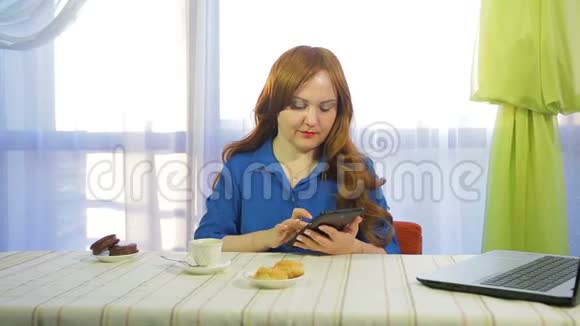 一个棕色头发的女人在一张桌子上的咖啡馆里工作拿着一块药片喝咖啡视频的预览图