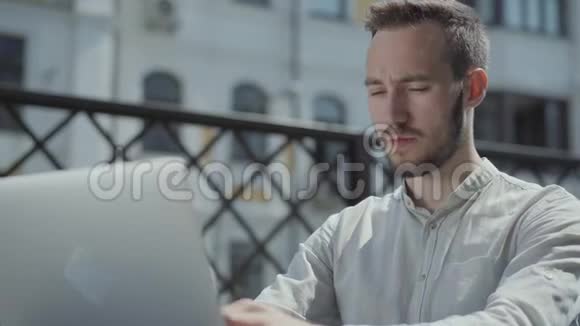 肖像胡子的年轻人坐在笔记本电脑前的露台上的桌子上工作自由职业概念视频的预览图