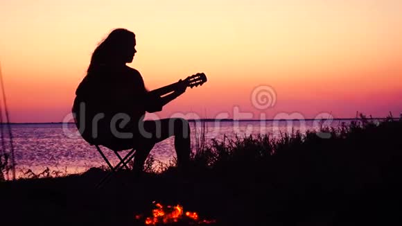 日落时分在海滩上玩吉他和篝火的小女孩视频的预览图