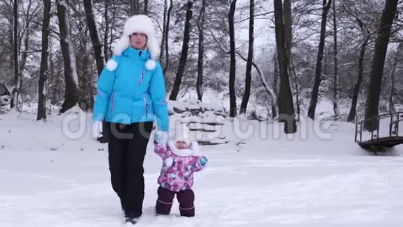 妈妈牵着幸福的小女儿的手沿着雪道走宝宝和妈妈在冬天散步妈妈带着孩子视频的预览图