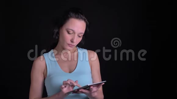 中年妇女在黑色背景下饶有兴趣地观看平板电脑的肖像视频的预览图