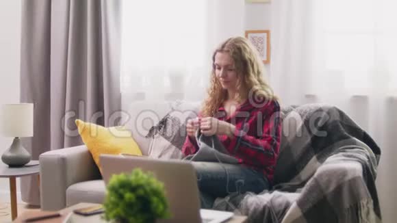 在舒适的家中坐在沙发上编织钩针衣服的中弹女子视频的预览图