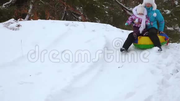 妈妈和女儿在冬天的雪碟上从高高的雪山上翻滚笑了起来快乐的母亲和小孩子视频的预览图
