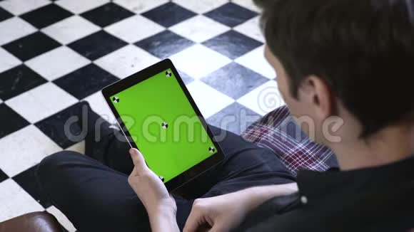 在景观模式下使用绿色模拟屏幕数字平板电脑从黑色衬衫年轻人的肩膀上观看视频的预览图