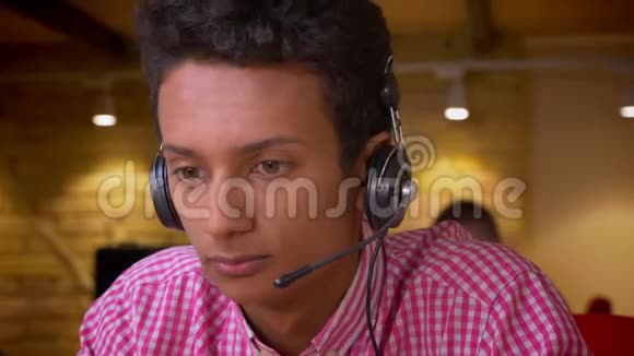 印度年轻员工戴着耳机的特写镜头在办公室里用笔记本电脑打电话视频的预览图
