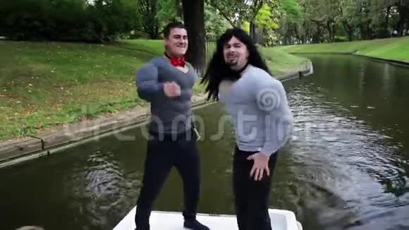 两个穿着假肌肉服装的英俊滑稽男子在船上唱歌视频的预览图