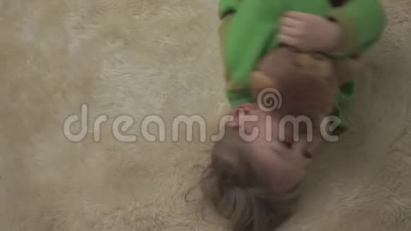 可爱的小男孩穿着绿色睡衣在地板上滚动毛茸茸的地毯拥抱泰迪熊快乐快乐的孩子视频的预览图