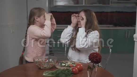 坐在厨房里的快乐的姐妹们围着一份蔬菜沙拉把黄瓜片涂在眼睛上视频的预览图