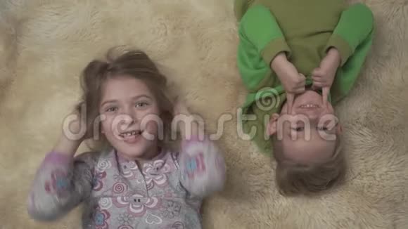 可爱的小孩子穿着睡衣躺在地板上铺着蓬松的地毯兄妹摸脸快乐的兄弟姐妹周末视频的预览图