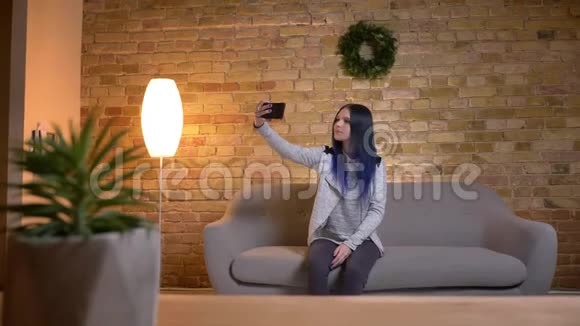 一位年轻迷人的白种人潮女在沙发上坐着一边打电话一边自拍特写镜头视频的预览图